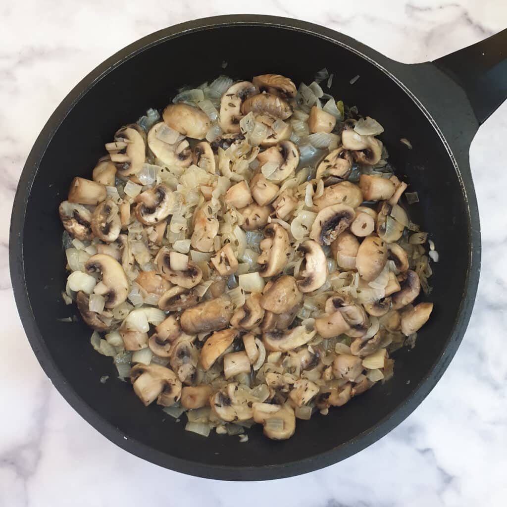 Flour stirred into mushrooms and onions in a frying pan.