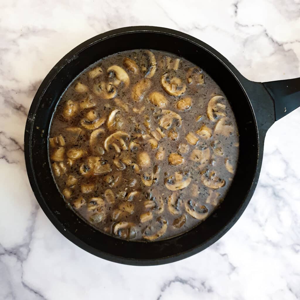 Stock thickening with mushrooms and onions in a frying pan.