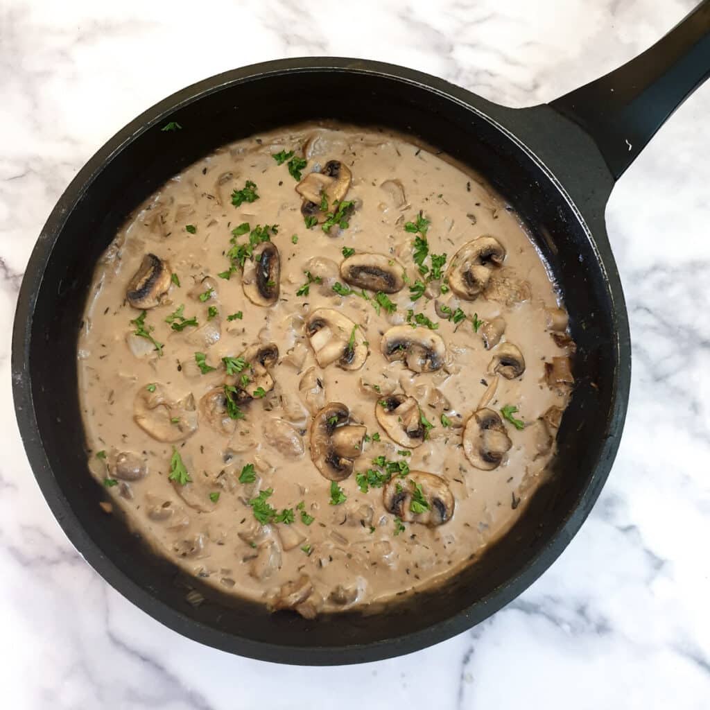 Cream stirred into marsala mushroom sauce in a frying pan.