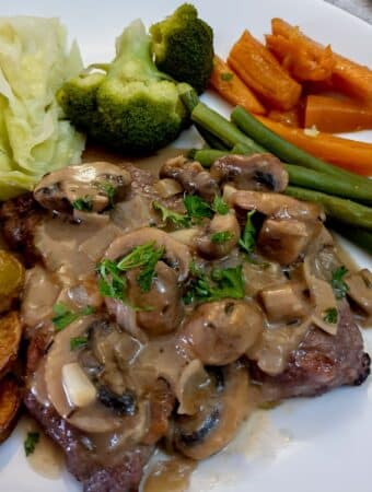 Marsala mushroom sauce poured over a steak on a plate with vegetables.