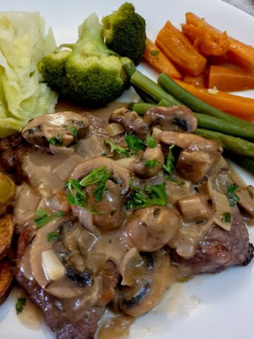 Marsala mushroom sauce poured over a steak on a plate with vegetables.