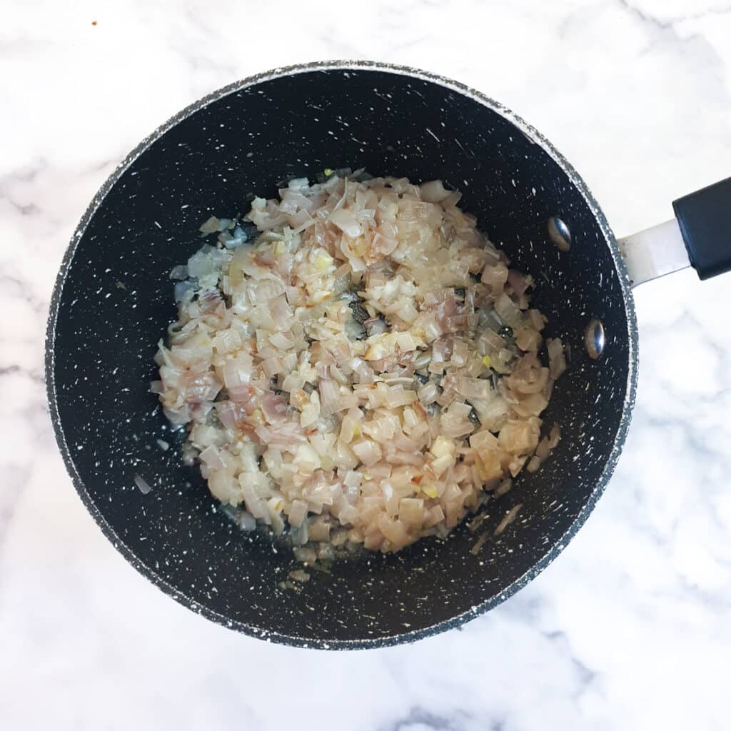 Translucent partly cooked shallots in a saucepan.