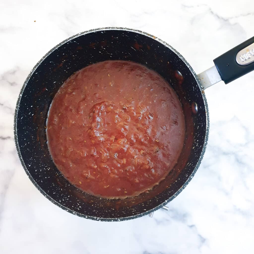 Thick and glossy marinara sauce in a saucepan.