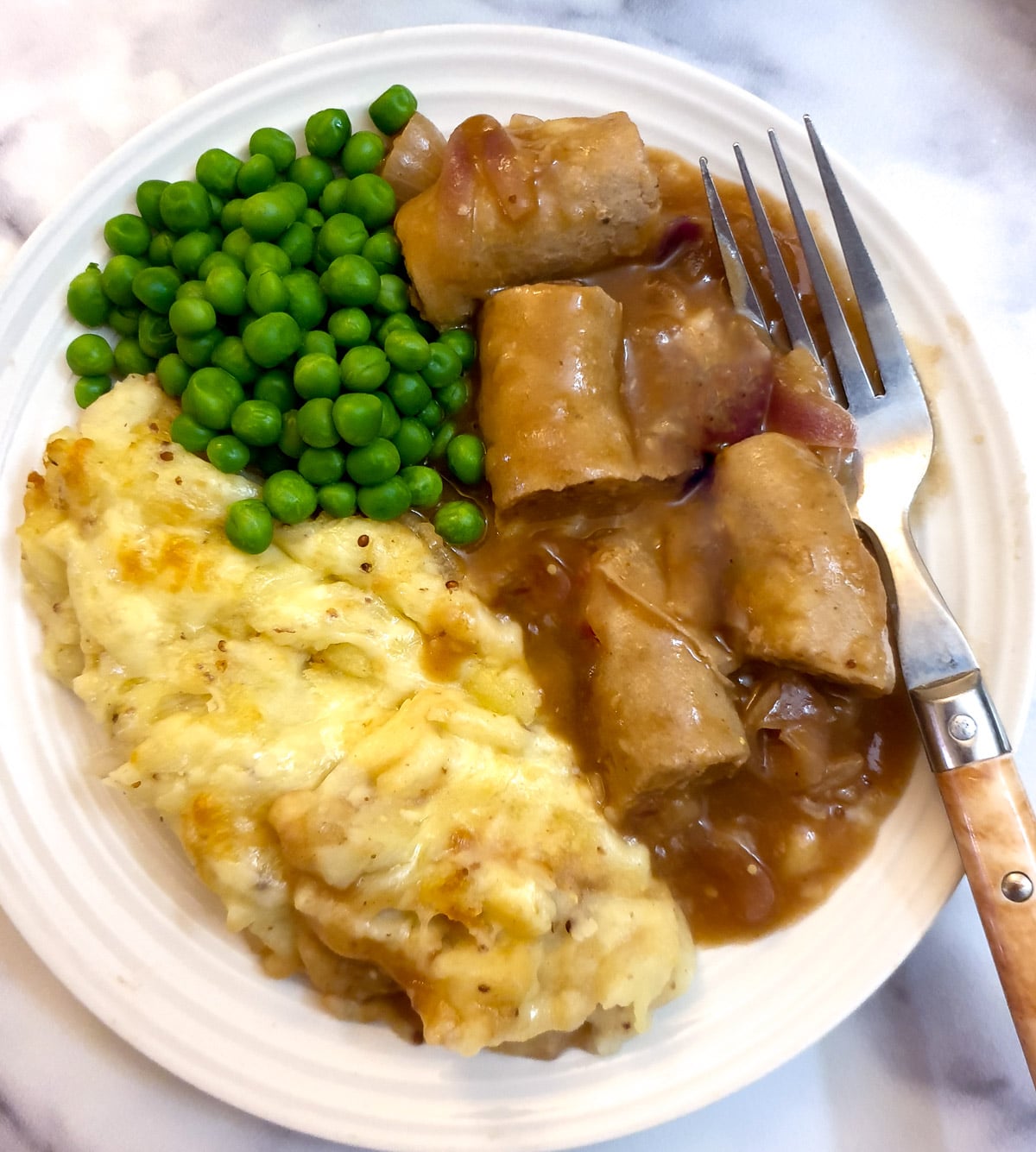 A plate of sausage cottage pie with a side of peas.