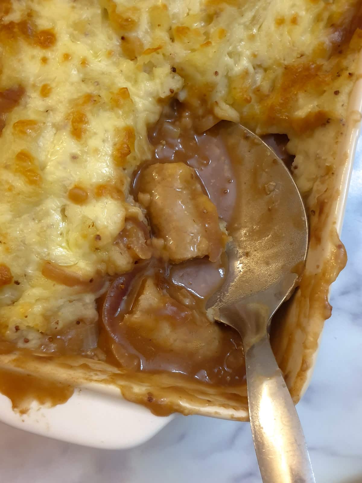 Two pieces of sausages on a spoon in the corner of a casserole dish.