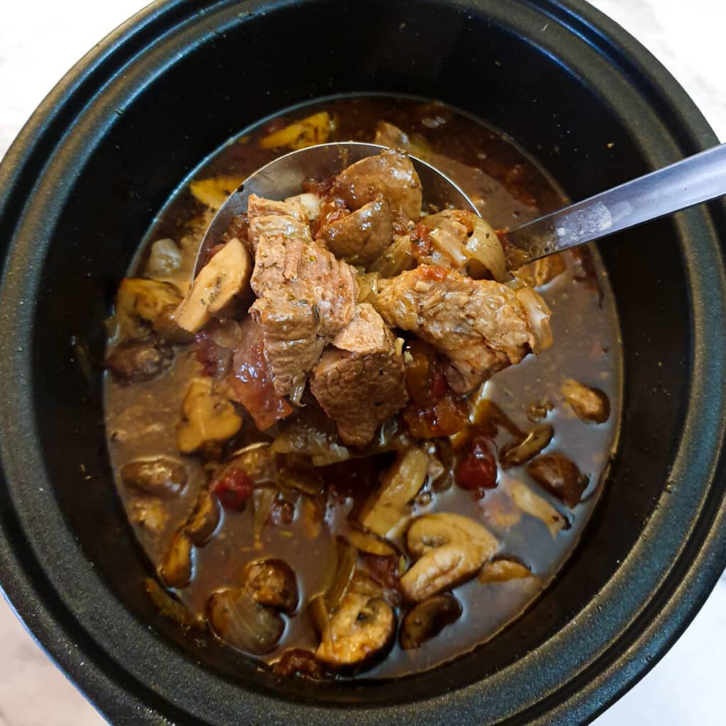 Cooked lamb ragu being removed from the slow cooker with a large spoon.