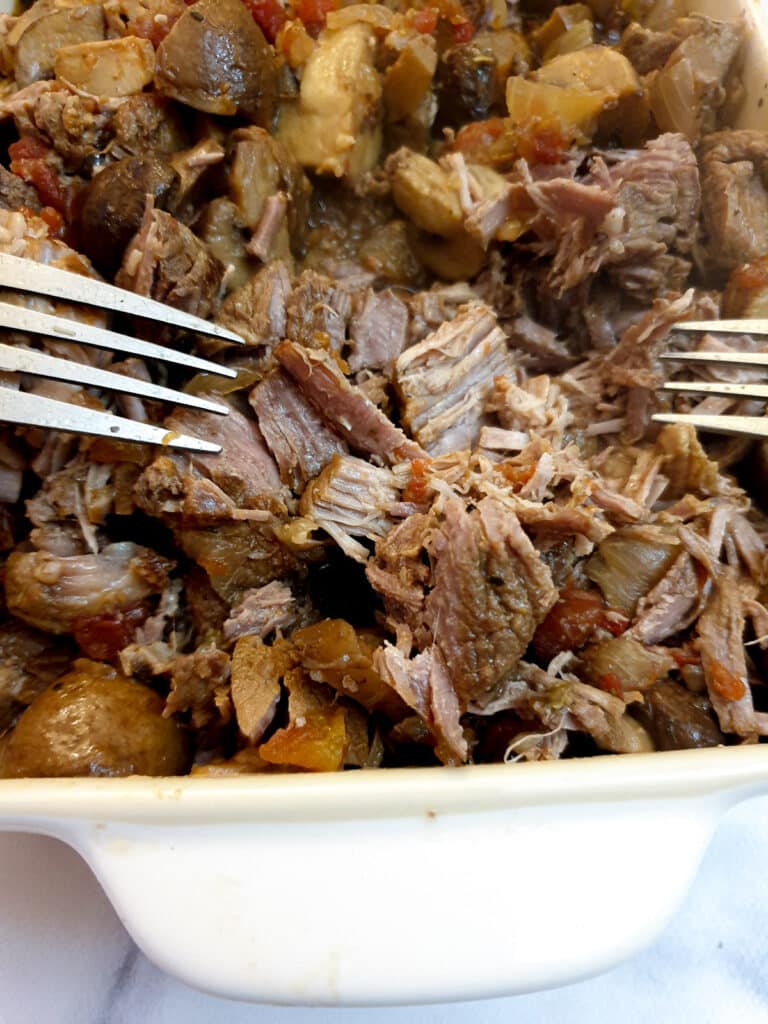 Close up of lamb ragu showing the meat being shredded with 2 forks.