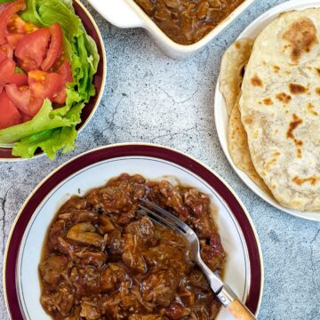 A plate of lamb ragu next to a plate of flatbread and a dish of salad.