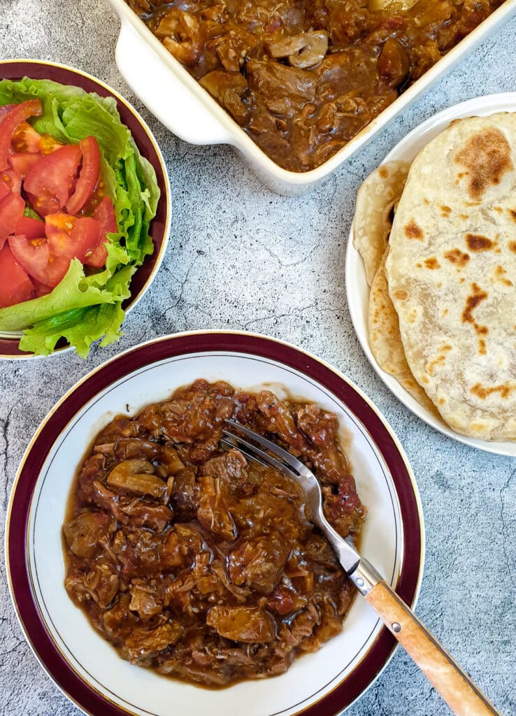 A plate of lamb ragu next to a plate of flatbread and a dish of salad.