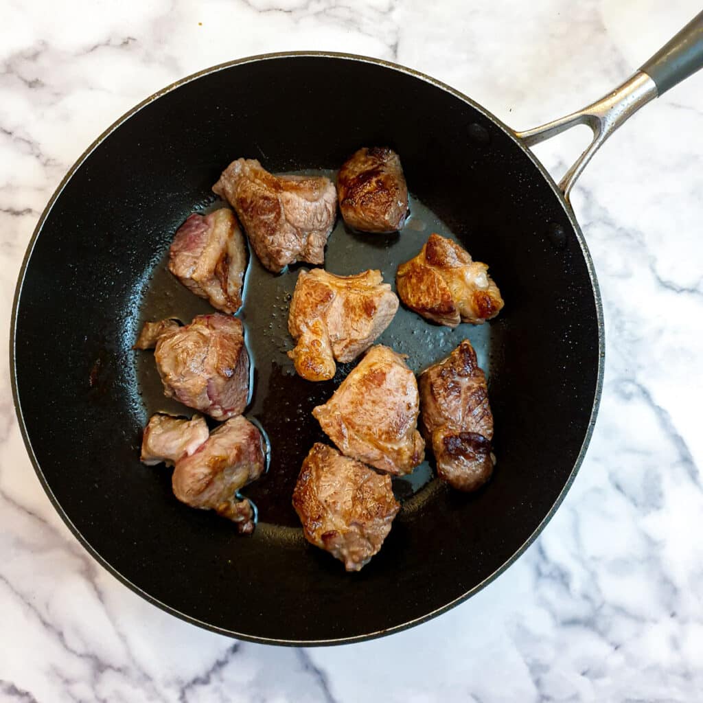 Pieces of lamb being browned in a frying pan.