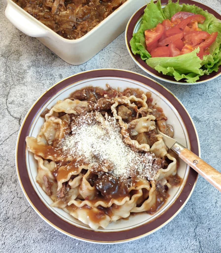 A dish of lamb ragu mixed with tagliatelle and topped with parmesan cheese.