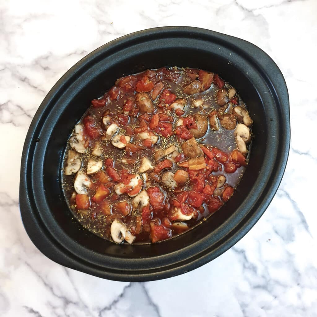 Tomatoes and stock added to the lamb ragu in a slow cooker.