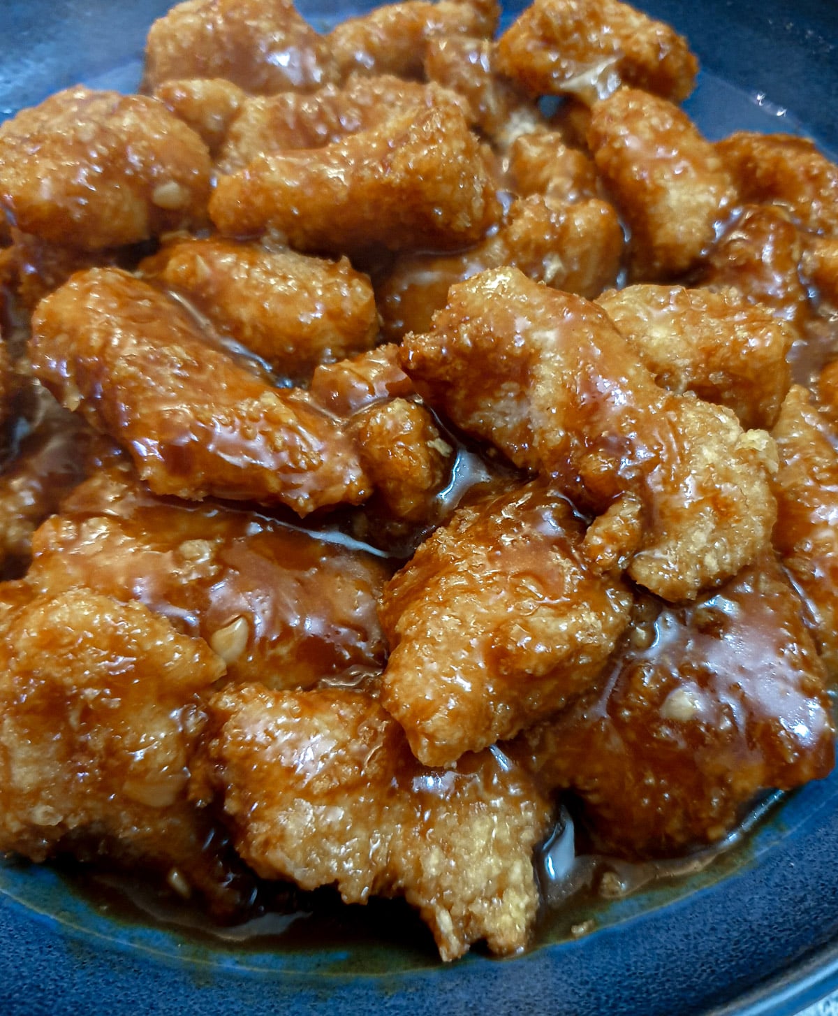 Sticky orange chicken pieces in a blue serving dish.
