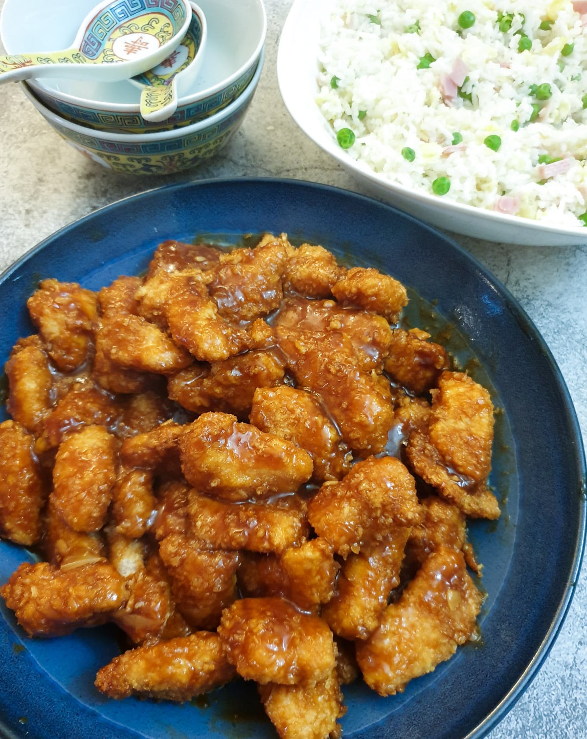 A dish of sticky orange chicke alongside a dish of Chinese fried rice.