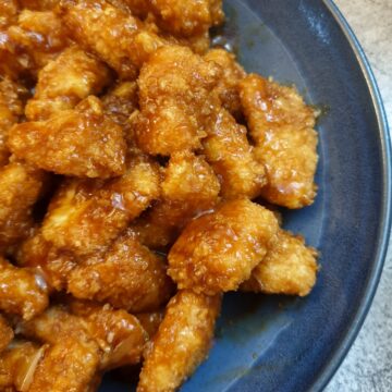 A blue serving dish filled with pieces of sticky orange chicken.