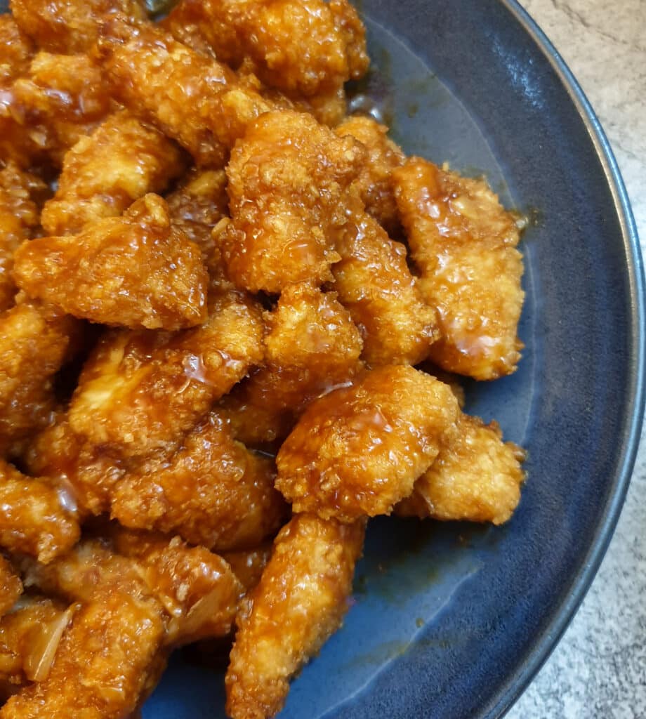 A blue serving dish filled with pieces of sticky orange chicken.