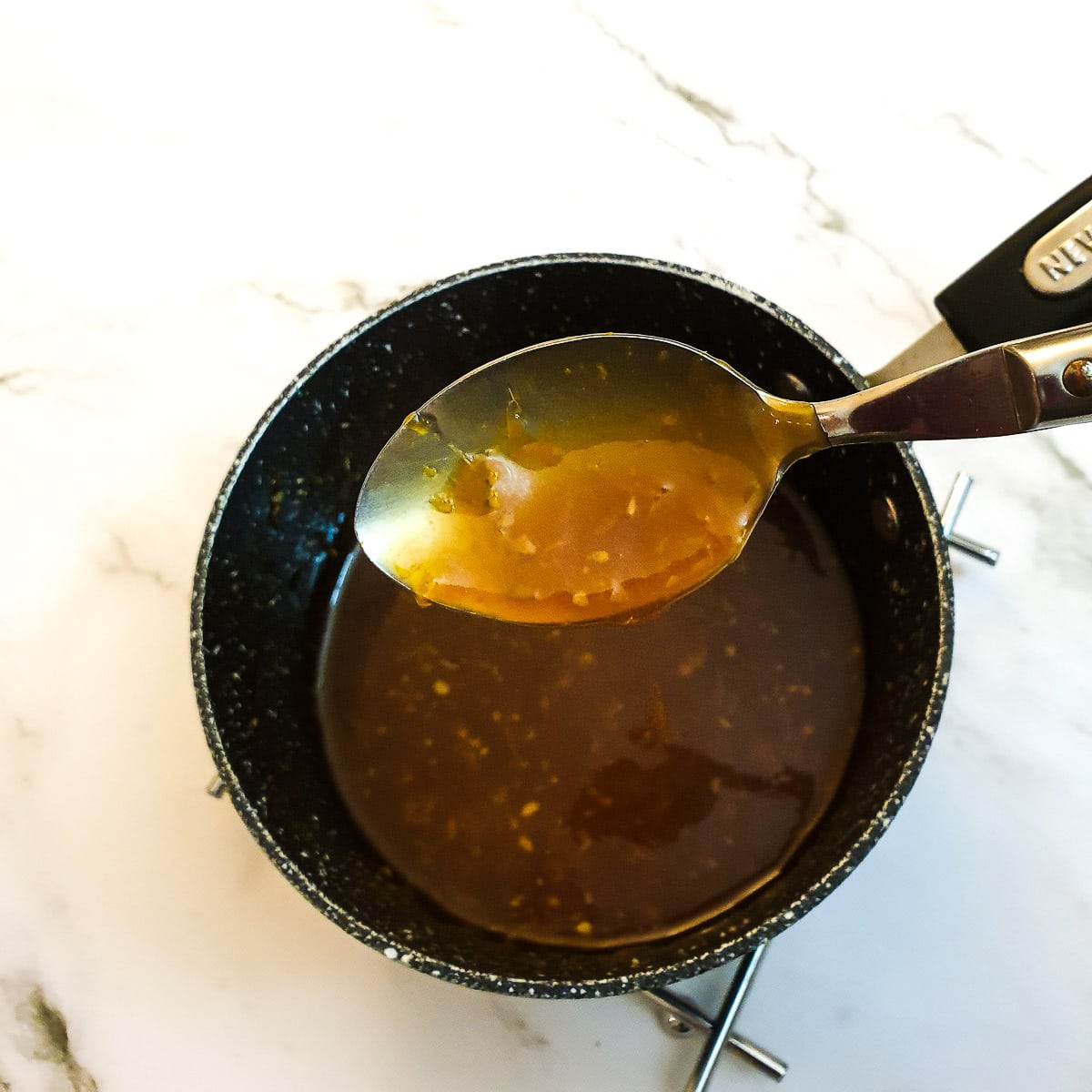 A spoon of orange sauce held over a saucepan of sauce.