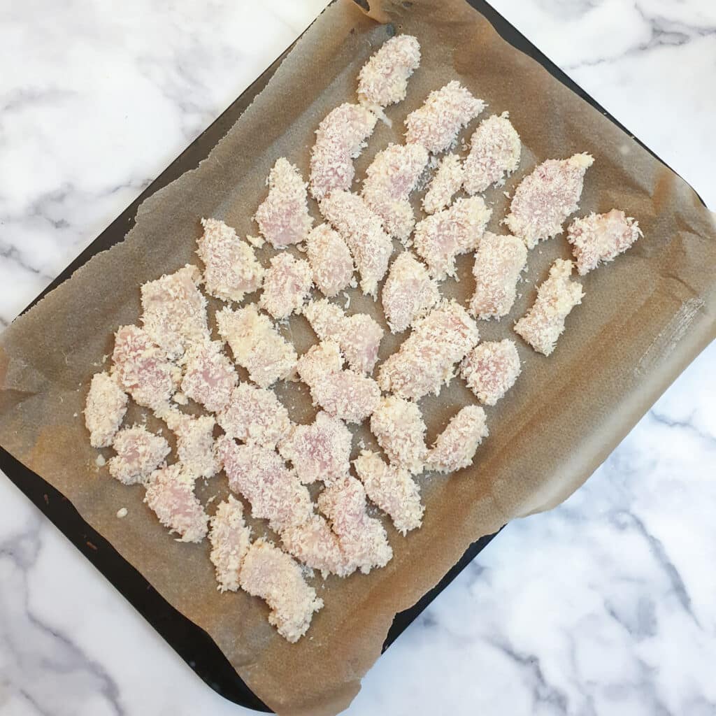 A baking tray with pieces of coated chicken.