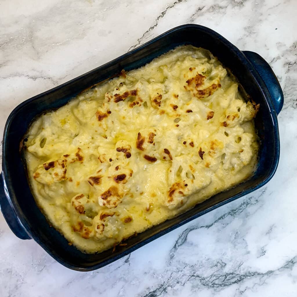 Baked and browned cauliflower cheese in a blue baking dish.