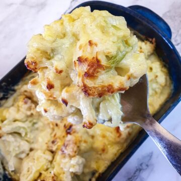 A spoonful of browned cauliflower cheese held over a serving dish.