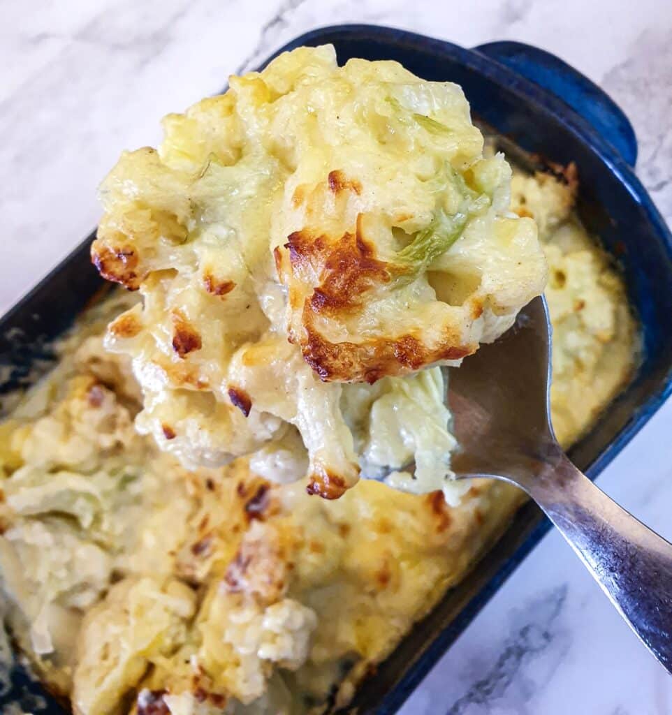 A spoonful of browned cauliflower cheese held over a serving dish.