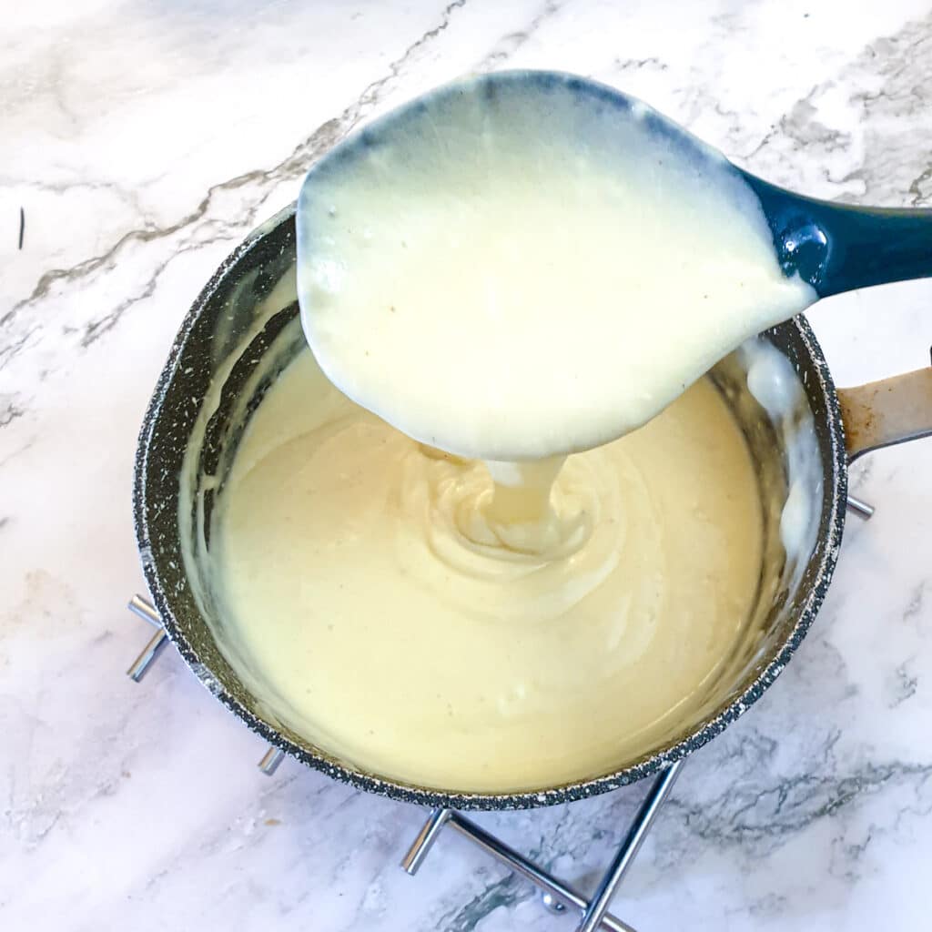 Thickened cheese sauce being spooned from a saucepan.