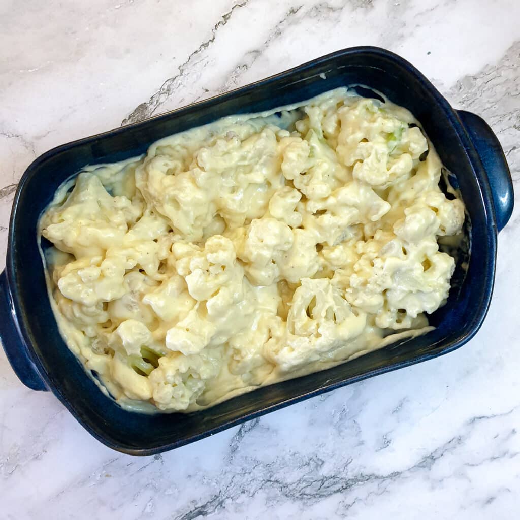 Cheese sauce mixed with steamed cauliflower in a blue baking dish.