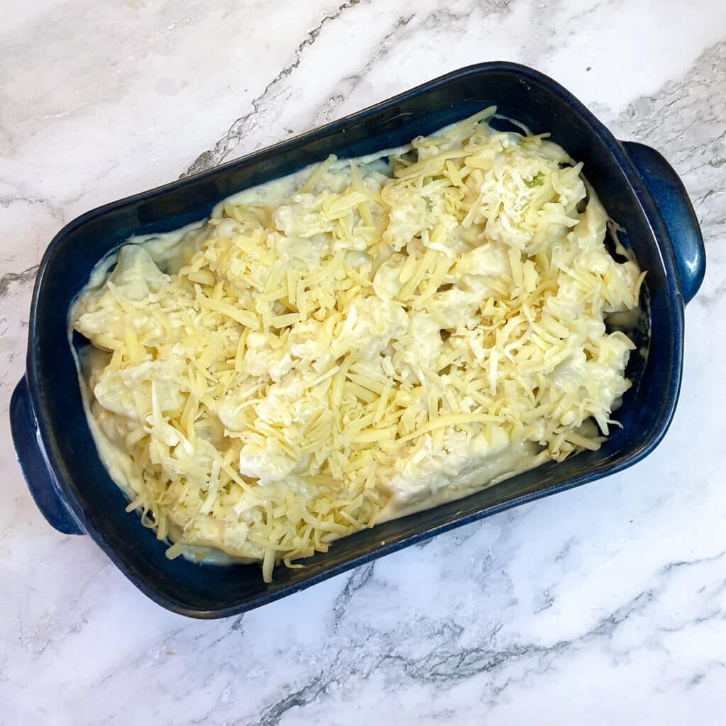 Grated cheese spread over cauliflower in a blue baking dish.