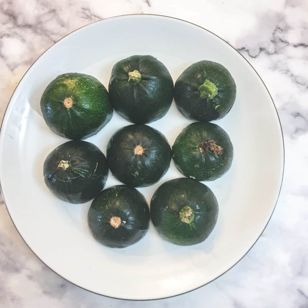 8 gem squash halves placed cut side down on a white plate.