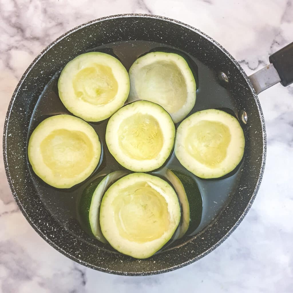 Gem squash halves in a pot of water.