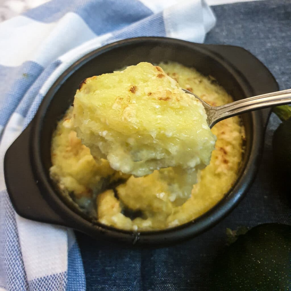 A spoonful of cheesy gem squash being lifted from a black serving dish.