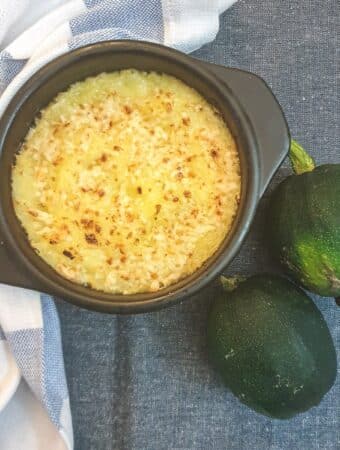 A dish of baked gem squash on a blue tablecloth next to 2 whole raw gem squash.