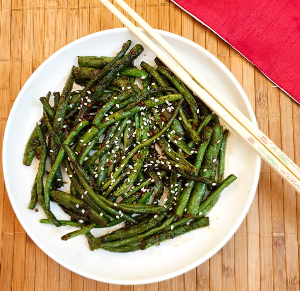 A white plate of Chinese garlic green beans garnished with sesame seeds.