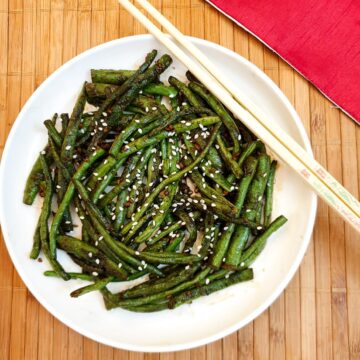 A white plate of Chinese garlic green beans garnished with sesame seeds.