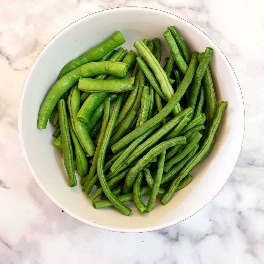 A white dish containing prepared green beans.