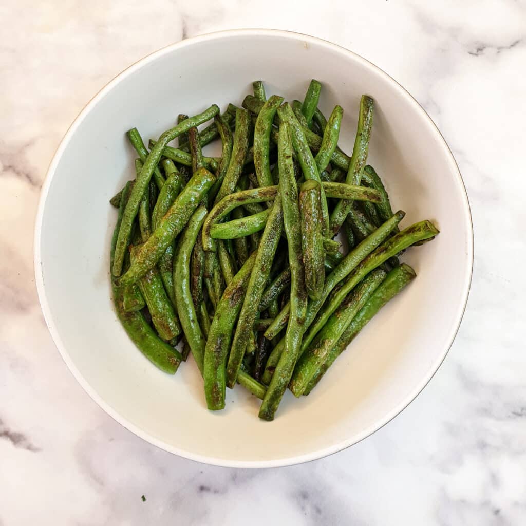 A white dish of charred green beans.