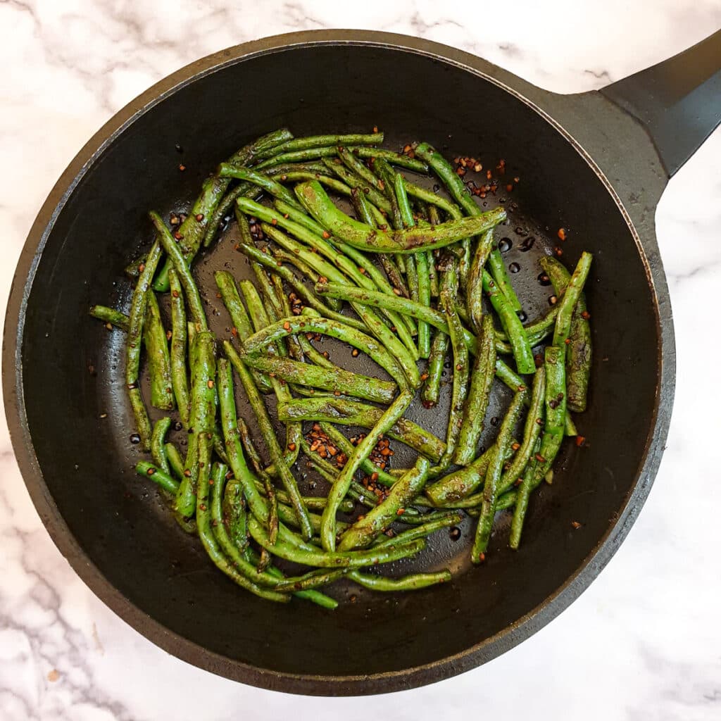 Green beans being mixed with sauce in a frying pan.