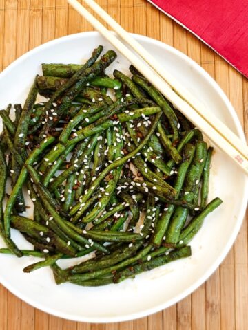 A white plate of Chinese garlic green beans garnished with sesame seeds.