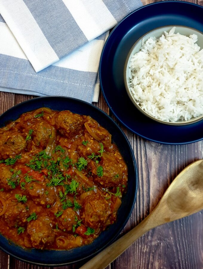 A dish of curried meatballs in onion gravy next to a bowl of white rice.