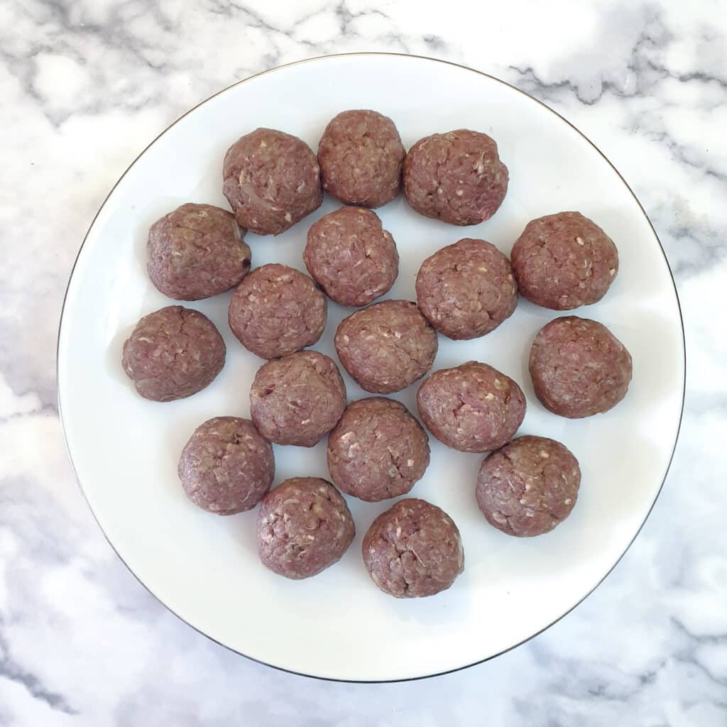 18 uncooked meatballs on a white plate.