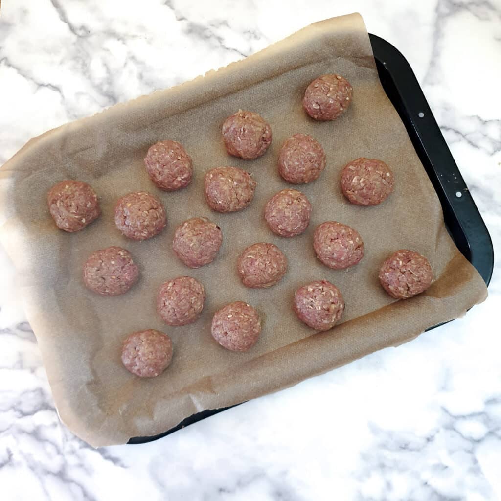 18 unbaked meatballs on a baking tray.