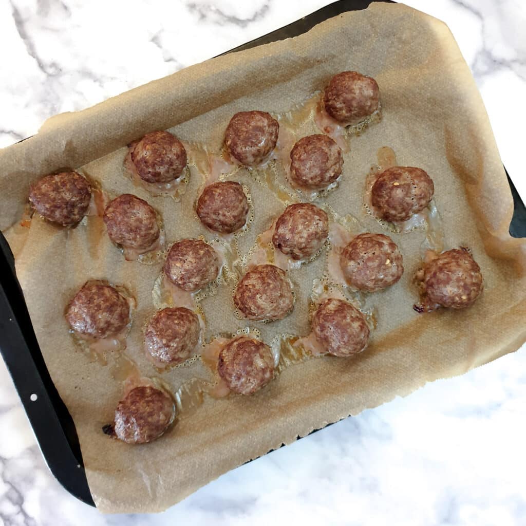 18 baked meatballs on a baking tray.