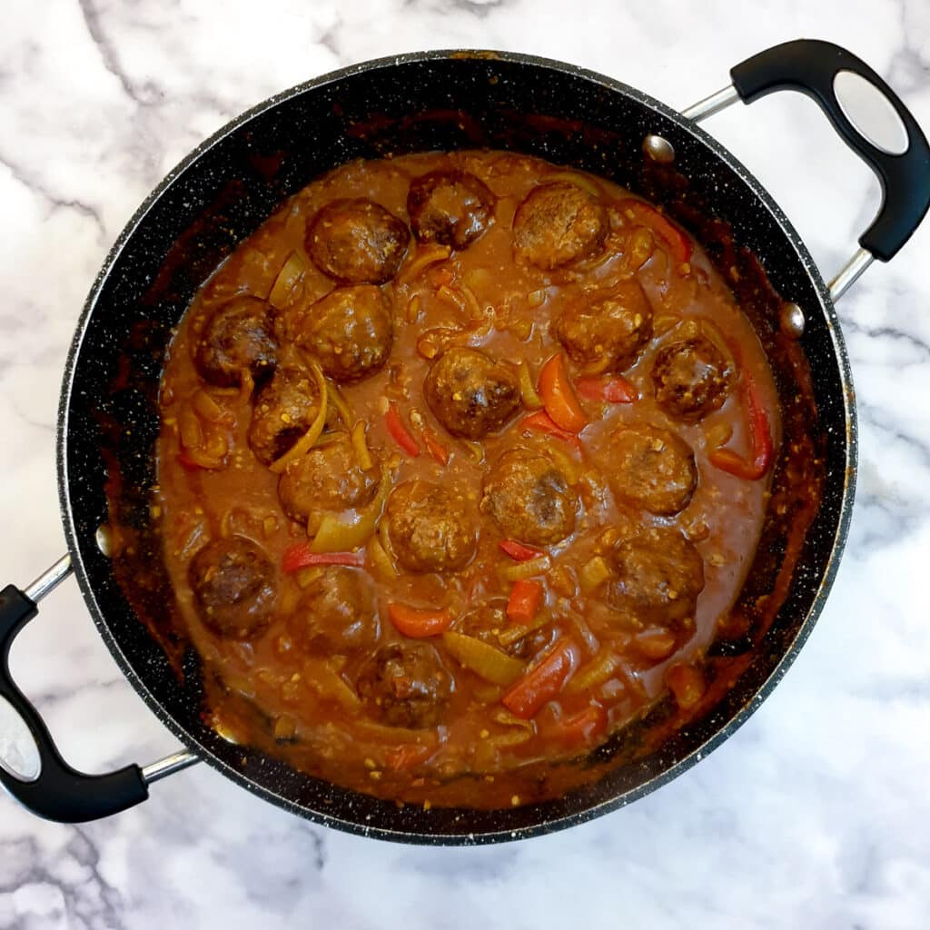 Baked meatballs added to curried onion gravy in a frying pan.