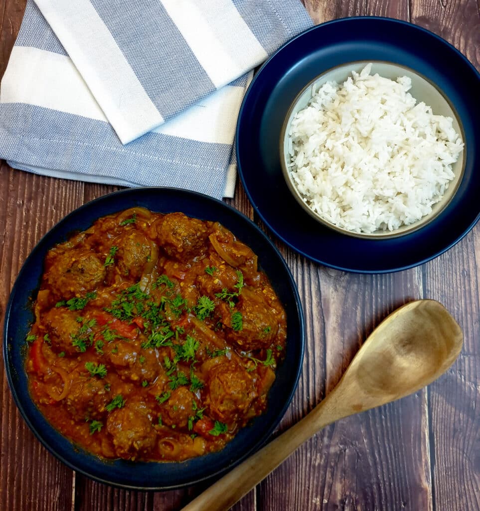 A dish of curried meatballs in onion gravy next to a bowl of white rice.