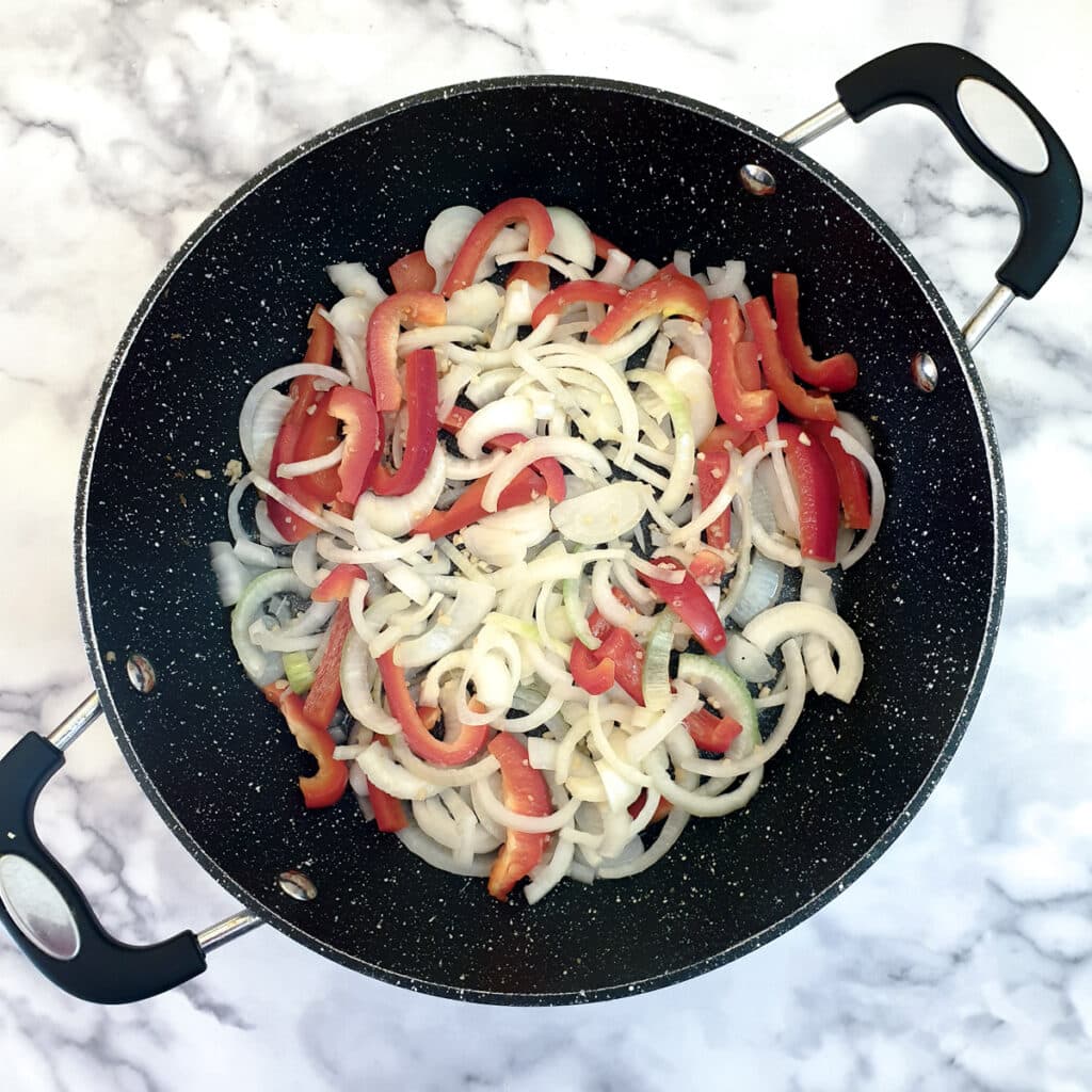 A frying pan containing sliced onions and red peppers.