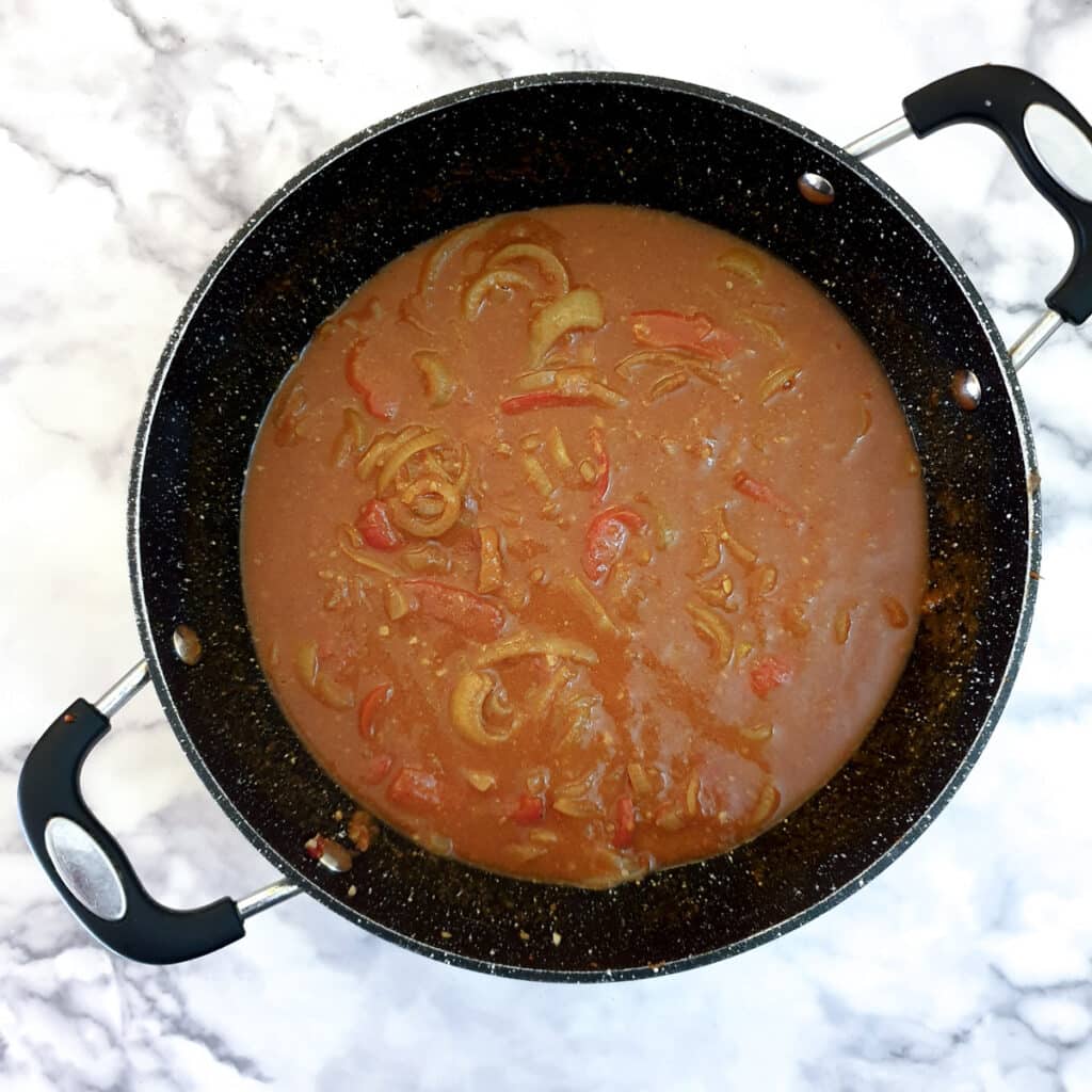 Stock and passata added to onions and peppers in a frying pan.