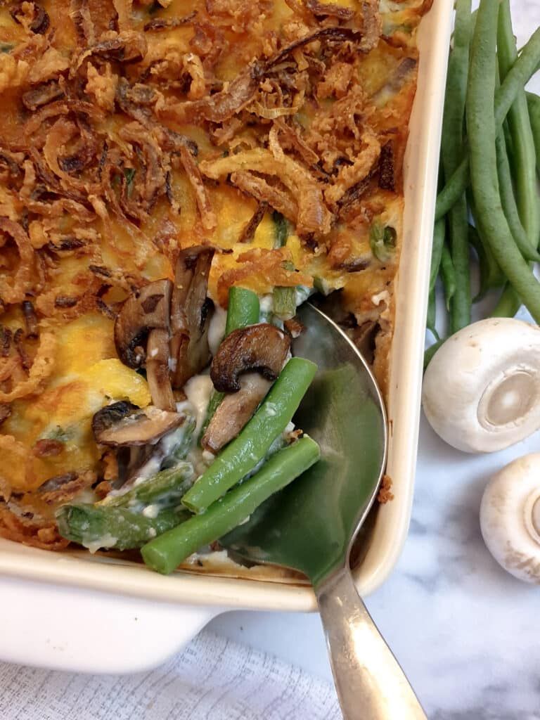 A green bean casserole with a corner removed to show the beans and mushrooms under the cheesy topping.