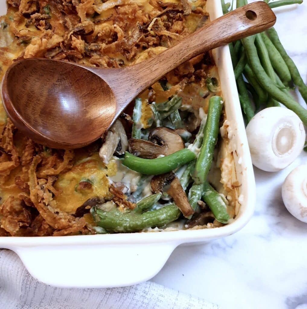 A green bean casserole in a serving dish with a wooden serving spoon.