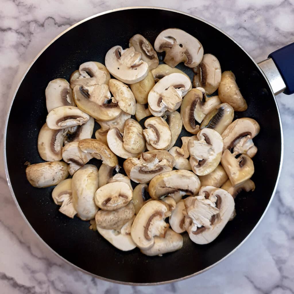 Raw sliced mushrooms in a frying pan.