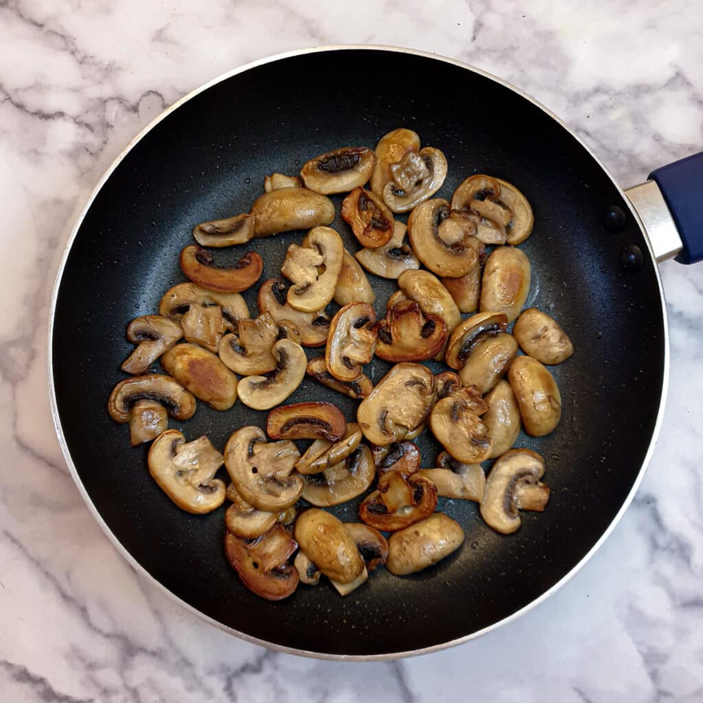 Browned sliced mushrooms in a frying pan.